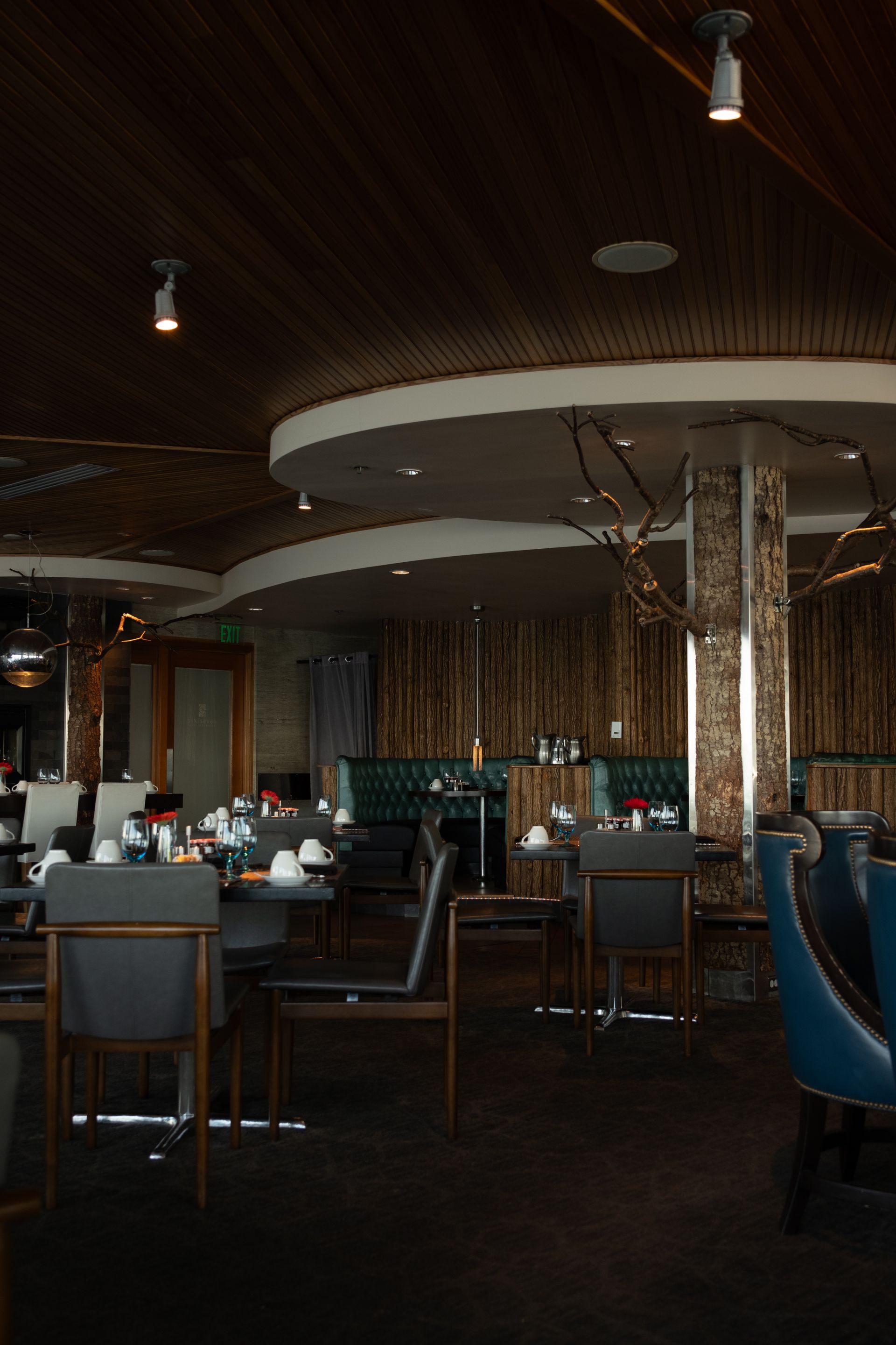 Salle de restaurant feutrée avec plafond courbe en bois, banquettes vertes et éclairage ponctuel.