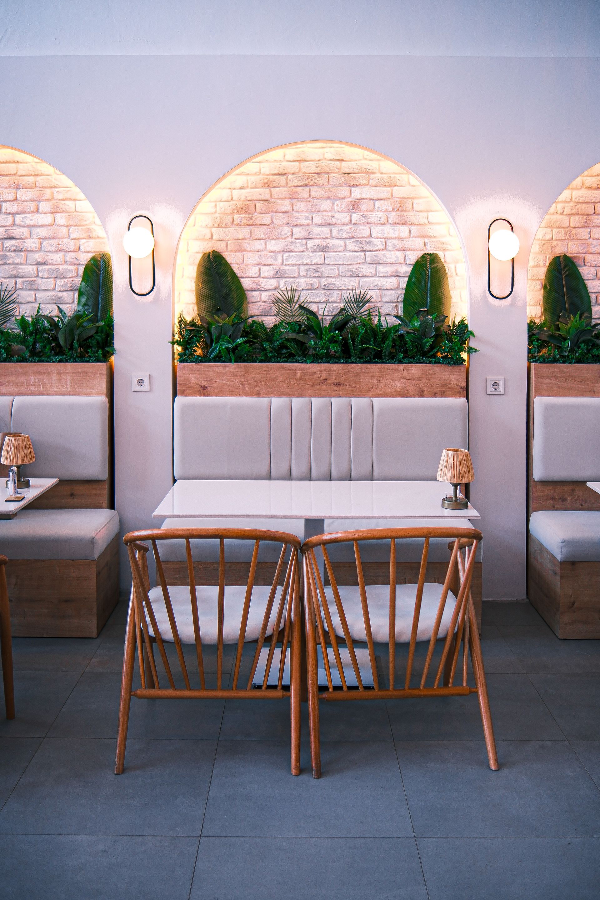 Banquette de restaurant avec niches murales en brique claire, plantes et appliques lumineuses.