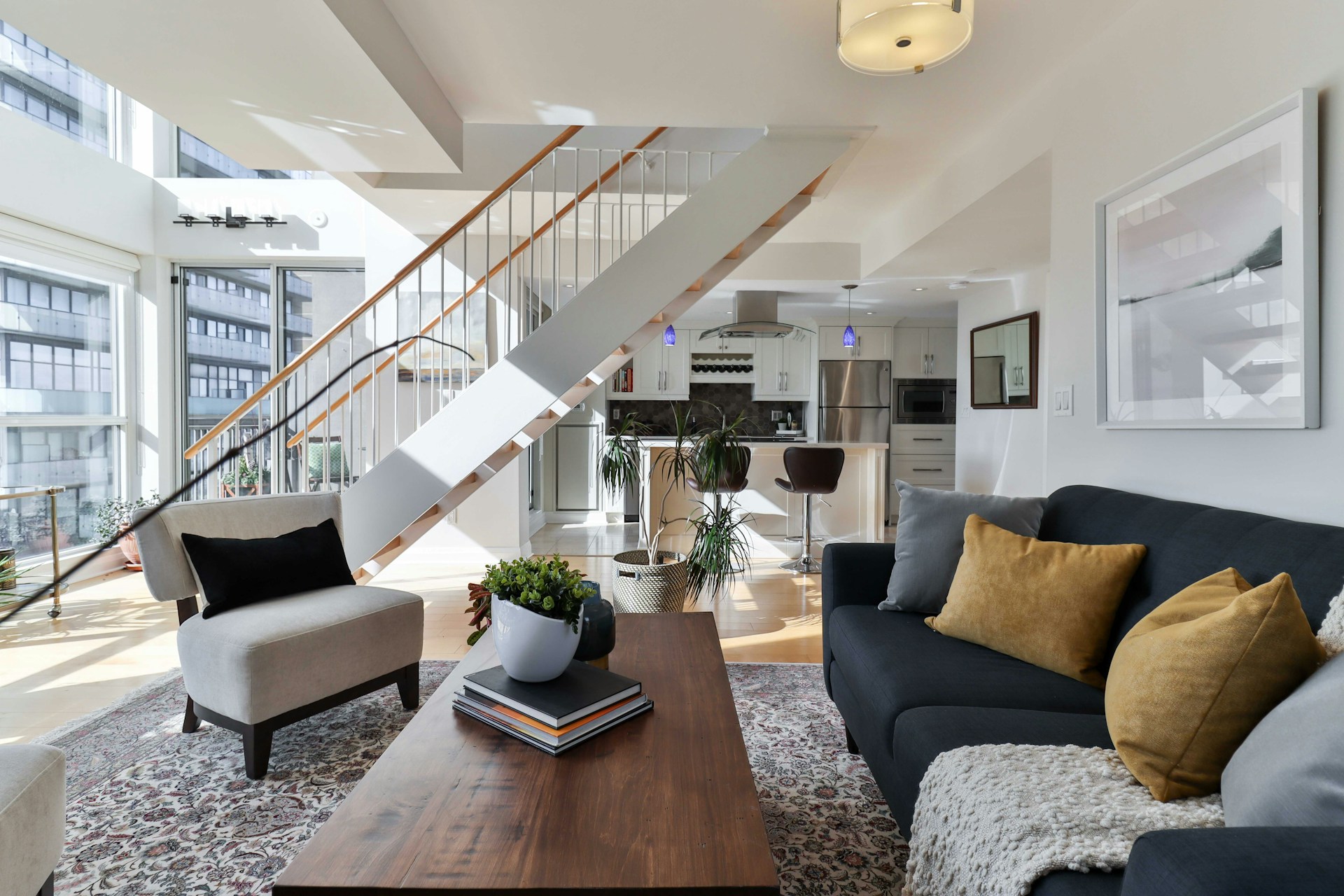 Espace salon ouvert sur une cuisine blanche avec escalier central et table basse en bois.